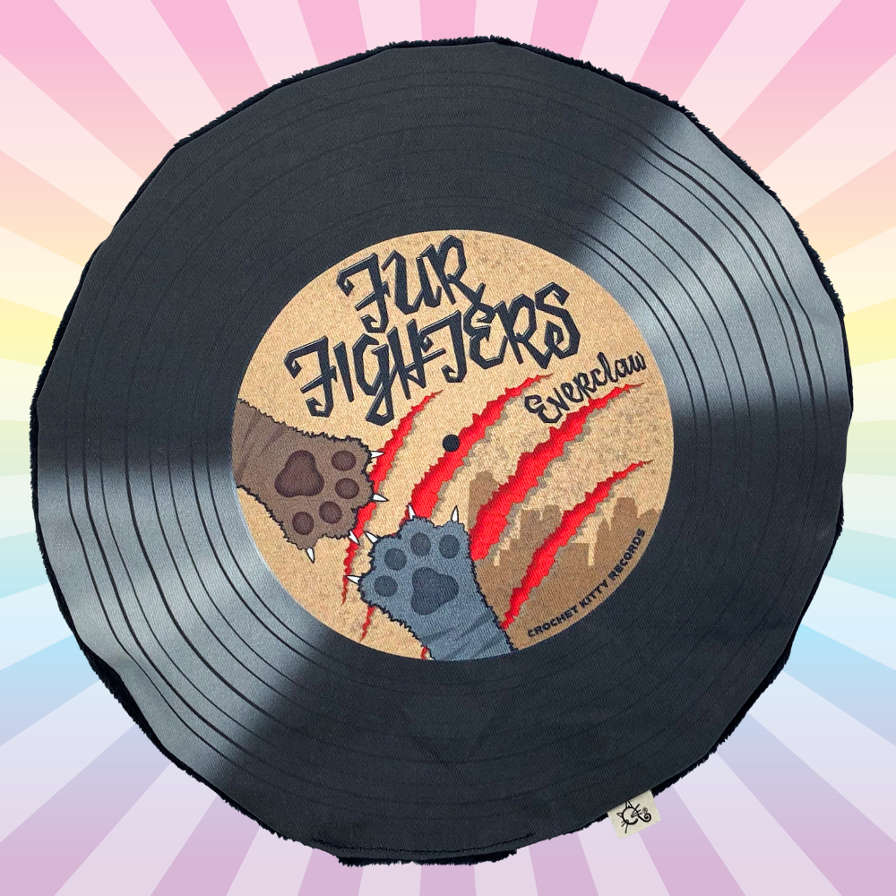 Black record plush cat toy with brown center with two cat paws fighting and the record reads "Fur Fighters" with a cat scratch in the background that is red in color. This record is on a rainbow ray background.