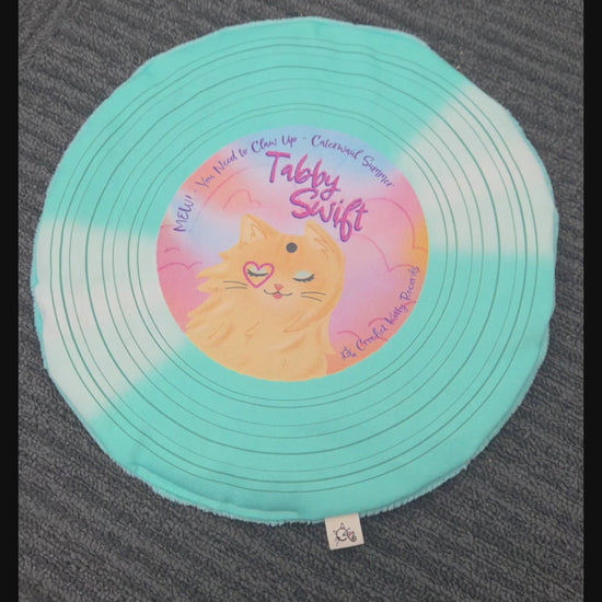 Hand pressing and scrunching a turquoise Tabby Swift record cat mat to demonstrate its crinkle.