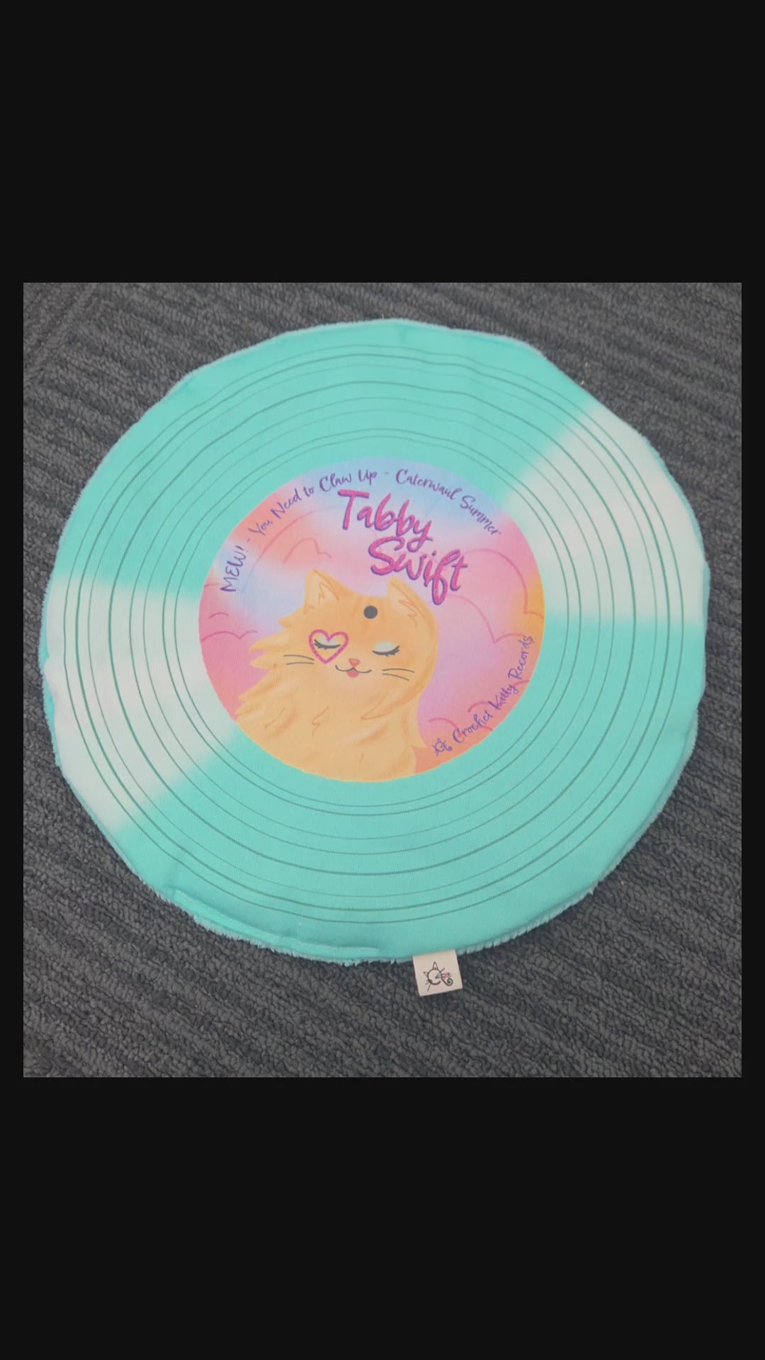 Hand pressing and scrunching a turquoise Tabby Swift record cat mat to demonstrate its crinkle.