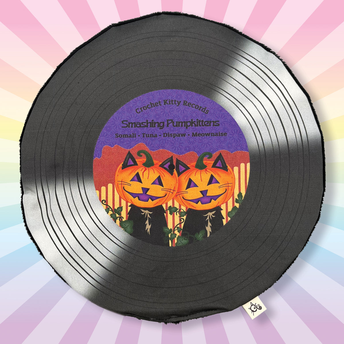 A round black vinyl record pillow with a colorful Halloween graphic on the label, featuring two smiling jack-o'-lantern faces and the text 'Crochet Kitty Records' and 'Smashing Pumpkittens'. The background is a pastel rainbow sunburst.